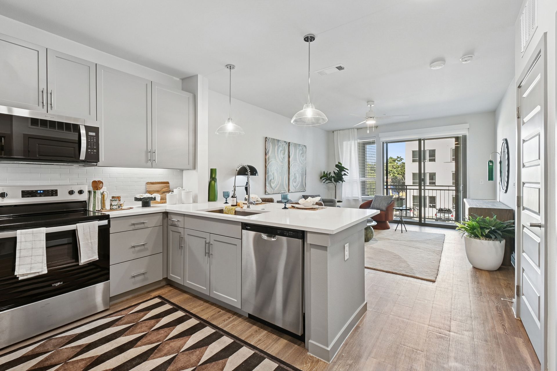 Bright modern kitchen and living area with gray cabinets, island, stainless appliances, and balcony view