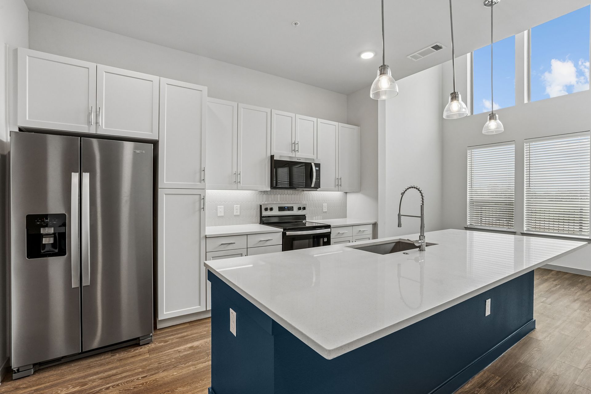 Modern white kitchen with stainless appliances and a blue island with a marble countertop