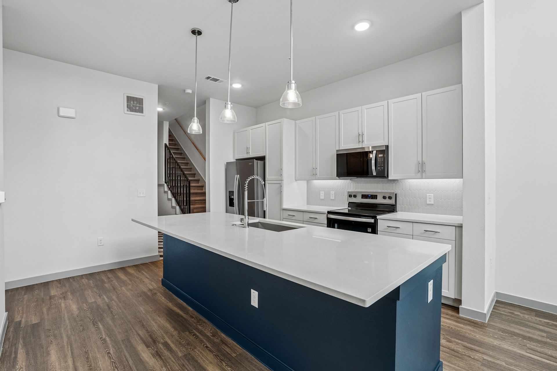 Modern kitchen with white cabinets, stainless appliances, blue island, and pendant lights