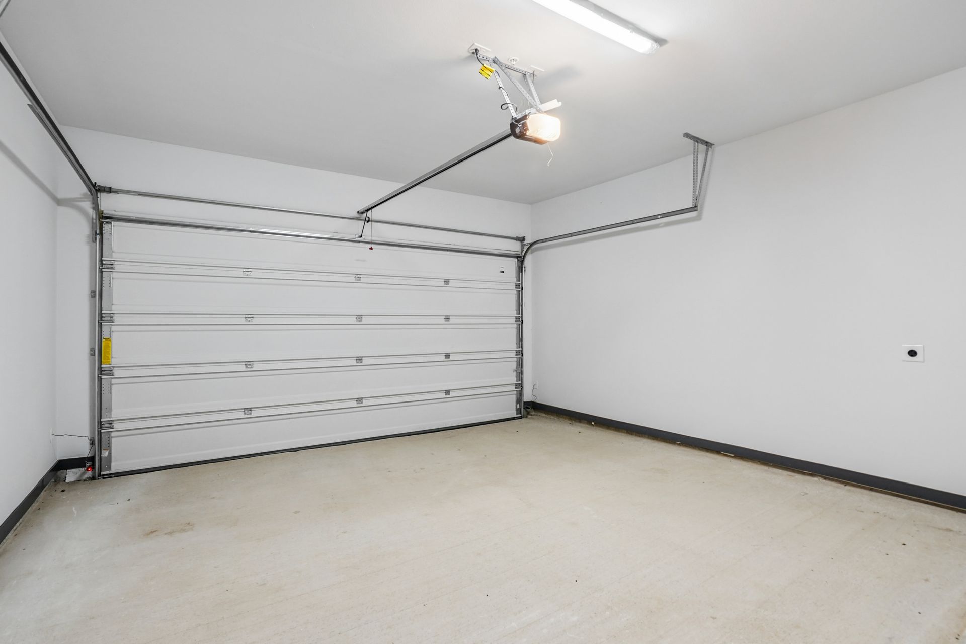 Empty white garage with closed door, concrete floor, and ceiling-mounted opener
