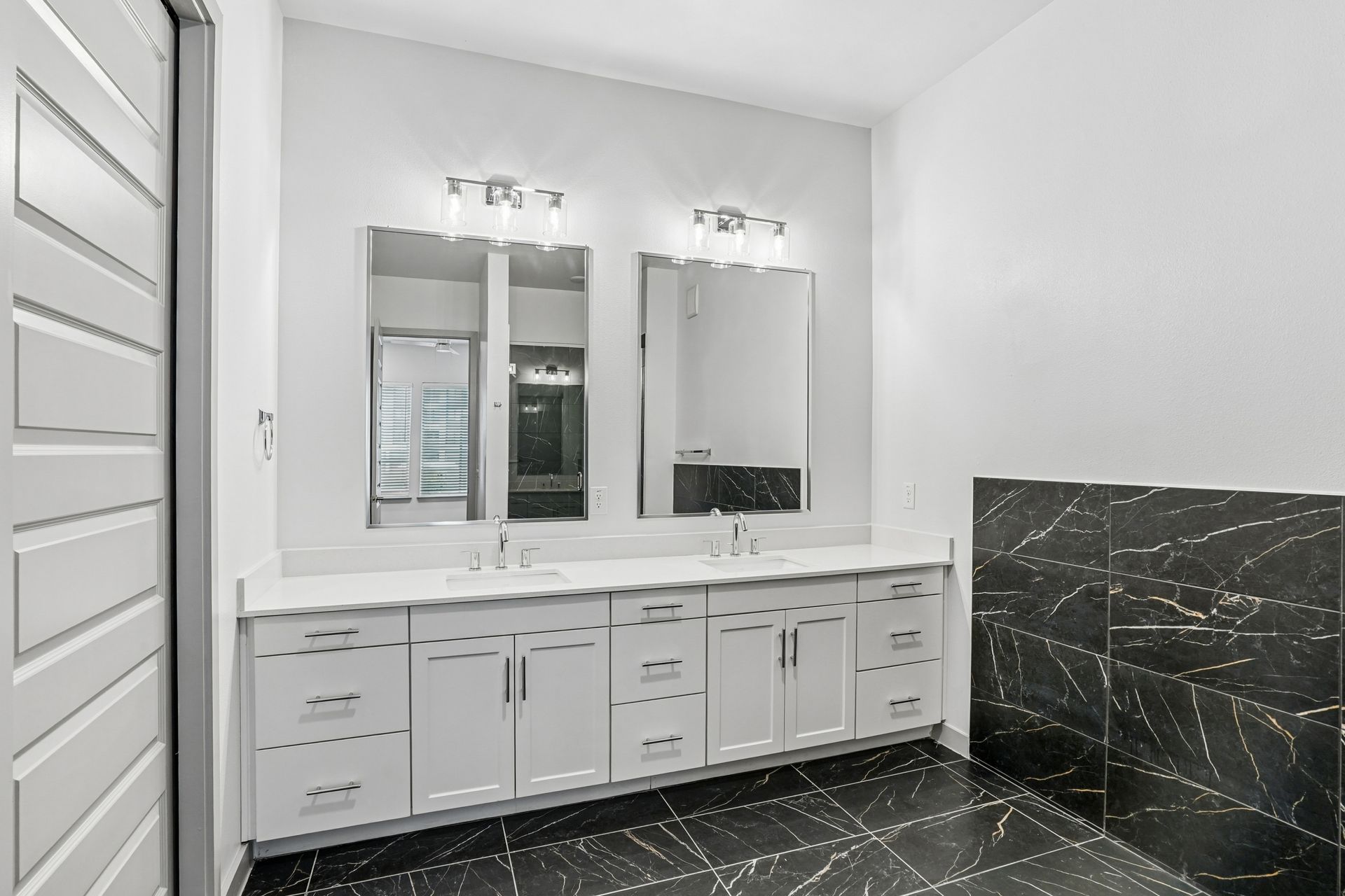 Modern bathroom vanity with double mirrors, white cabinets, and black marble tile accents
