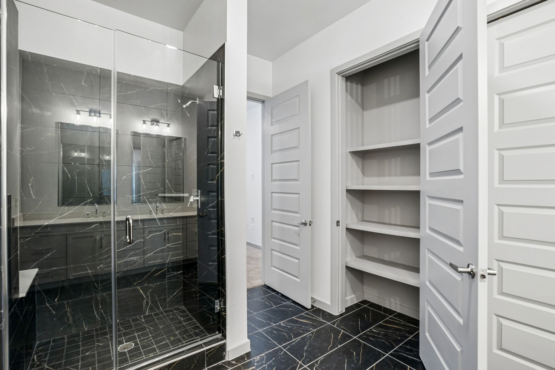 Modern bathroom with glass shower, black tile floor, and built-in white closet shelves