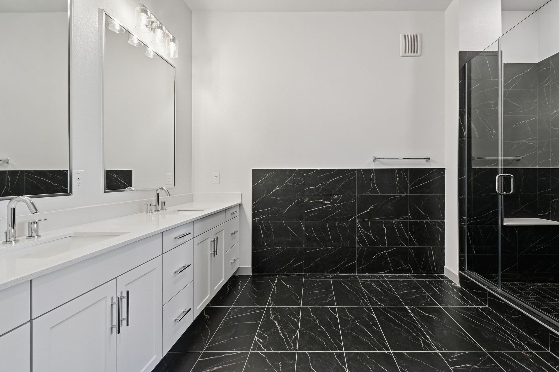 Modern bathroom with white vanity, mirrors, and black marble tile floor and shower walls