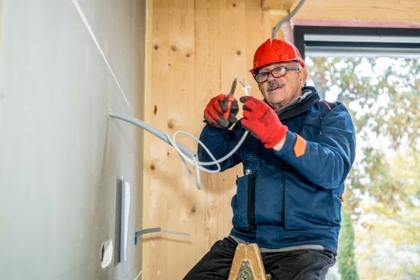 Worker in red hard hat wiring an outlet inside a partially finished room.