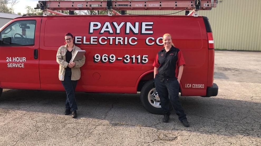 Two people standing beside a red Payne Electric Co. service van in a gravel lot