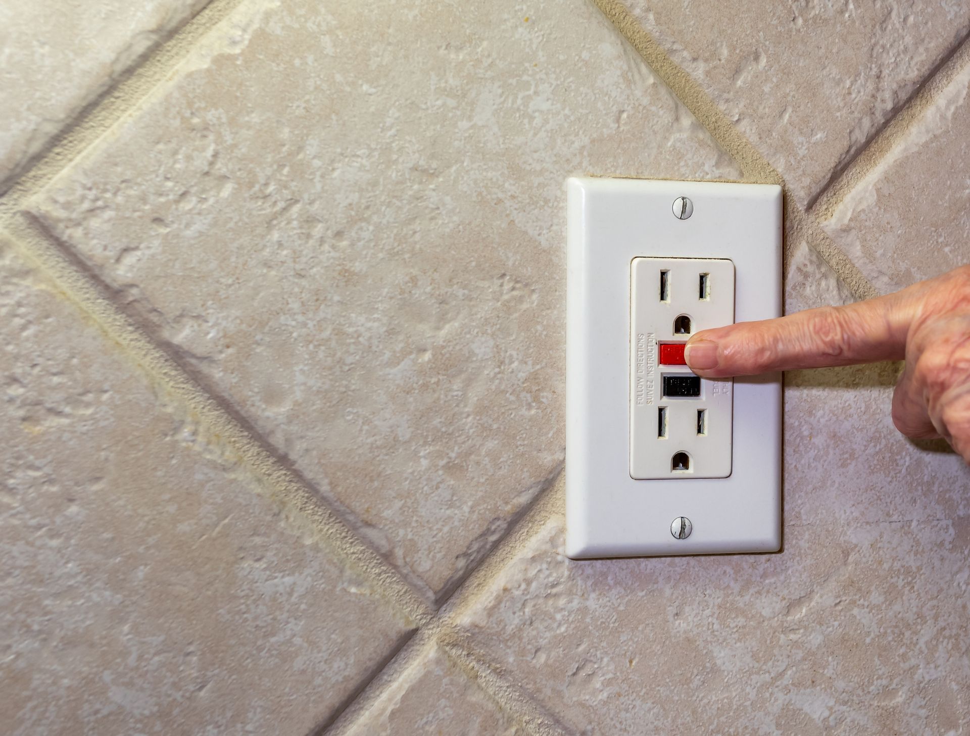Finger pressing a red reset button on a white GFCI outlet Finger pressing a red reset button on a white GFCI outlet