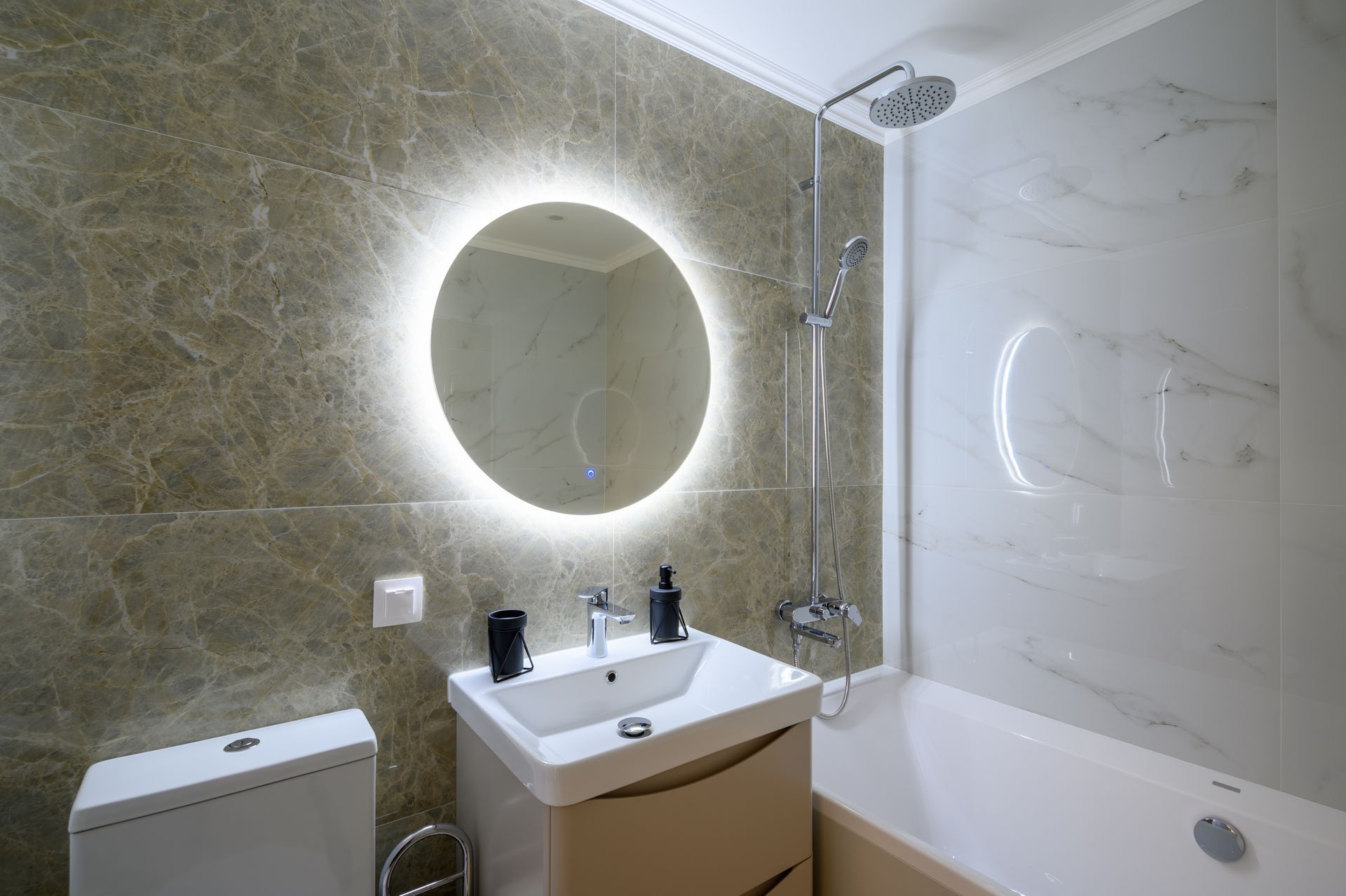 Modern bathroom with lit round mirror, sink, toilet, and bathtub with shower panel Modern bathroom with lit round mirror, sink, toilet, and bathtub with shower panel