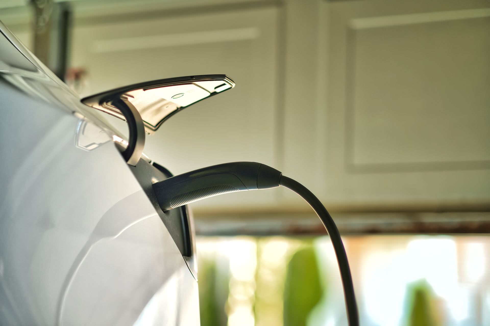 Black electric car charging plug connected to a white vehicle outdoors Black electric car charging plug connected to a white vehicle outdoors