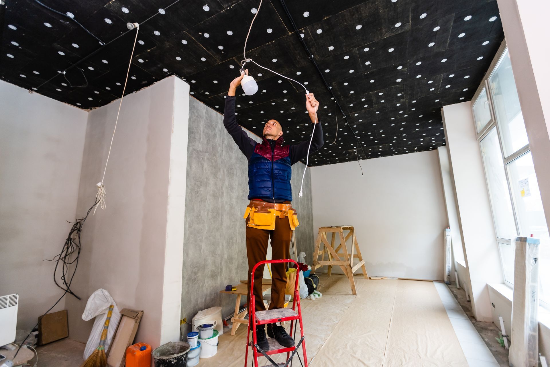 Worker on a red ladder installing lights on a black star-patterned ceiling in an unfinished room Worker on a red ladder installing lights on a black star-patterned ceiling in an unfinished room