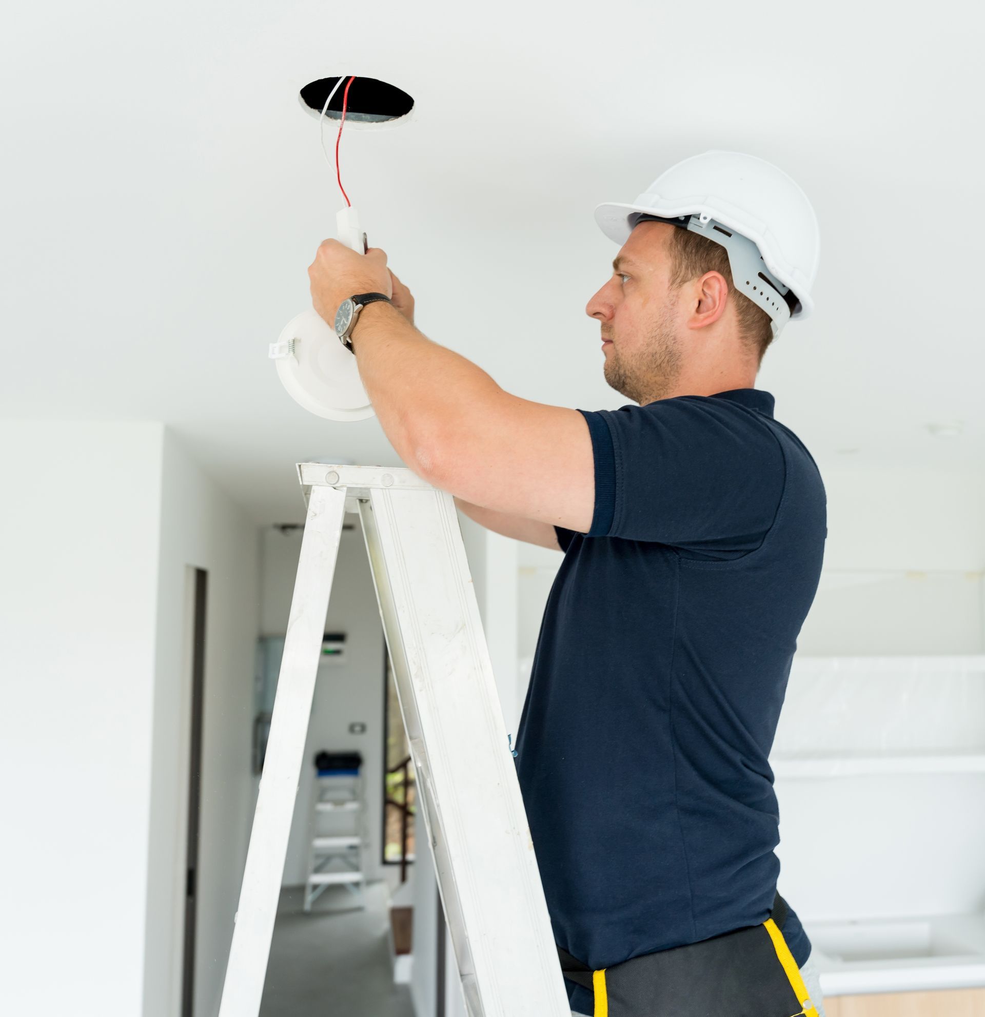 Worker on a stepladder installing a ceiling light fixture in a white room Worker on a stepladder installing a ceiling light fixture in a white room