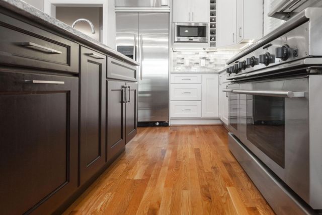 Wooden-floored kitchen with dark brown cabinets, stainless steel appliances, and white upper cabinets.