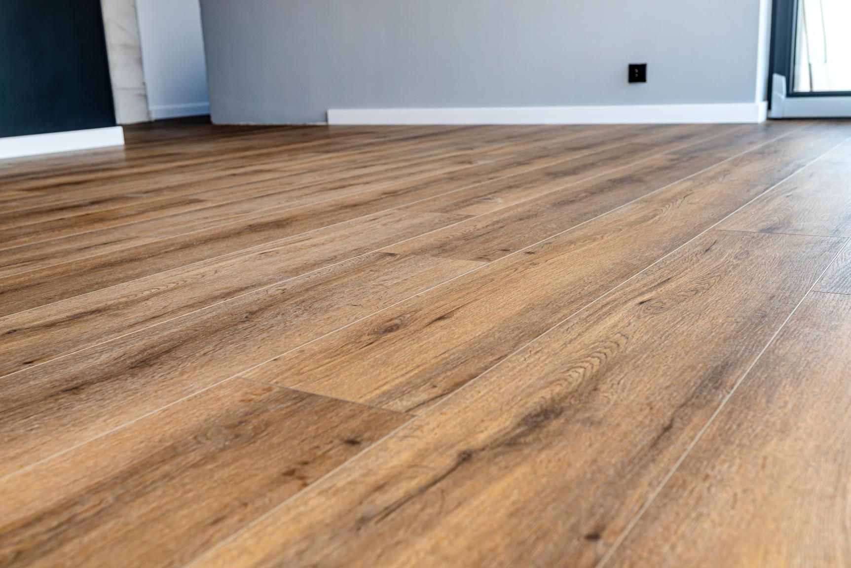 Close-up of light brown wood-look flooring in a room with gray and white walls.