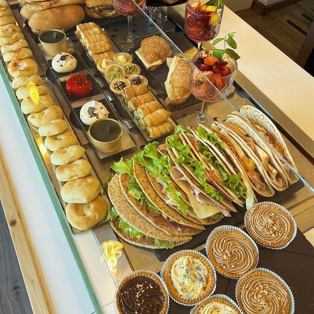 Una vetrina piena di vari panini, pasticcini salati, macedonie di frutta fresca e dessert monoporzione.