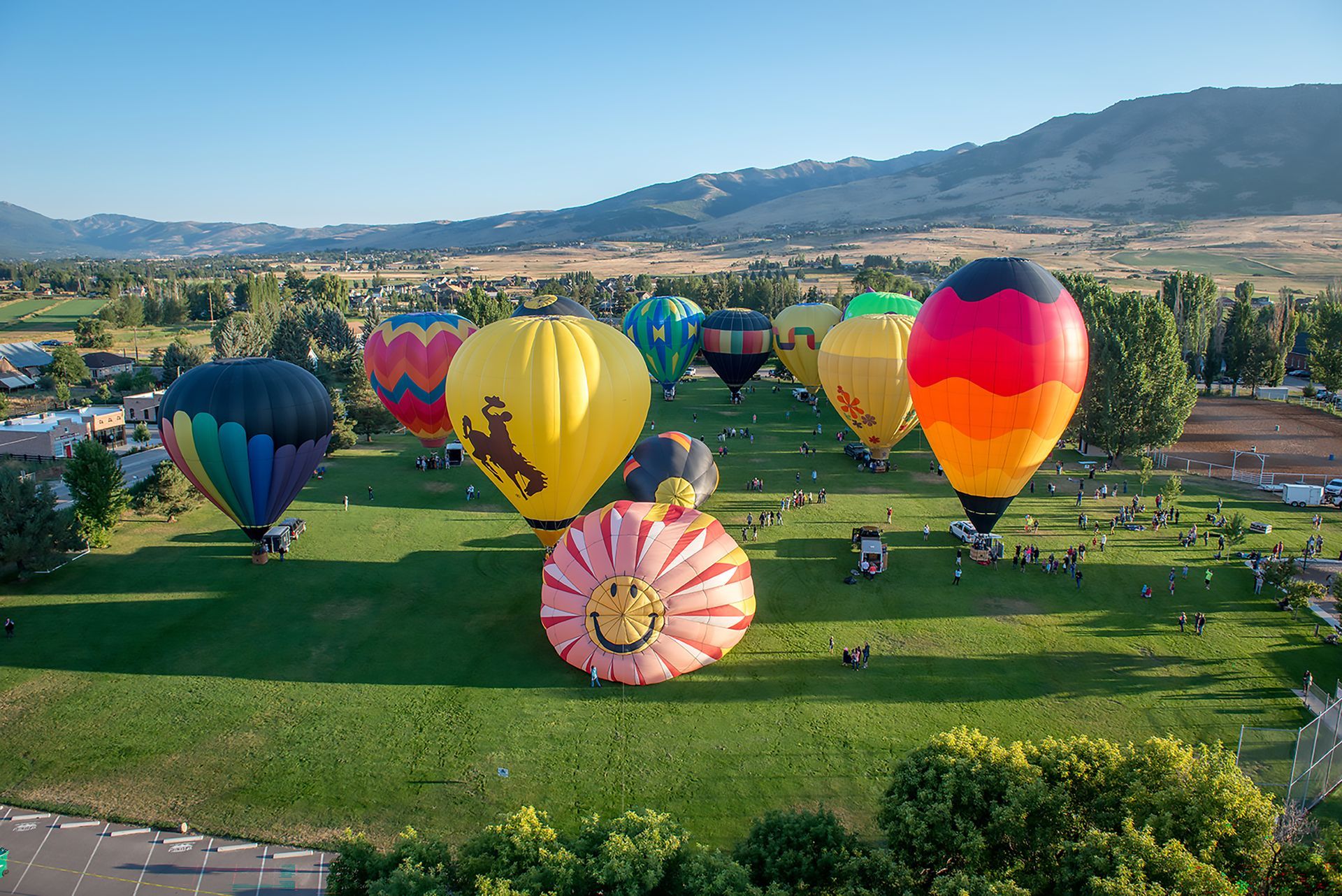 Hot air balloons tethered to the ground with green grass and mountains in the background.