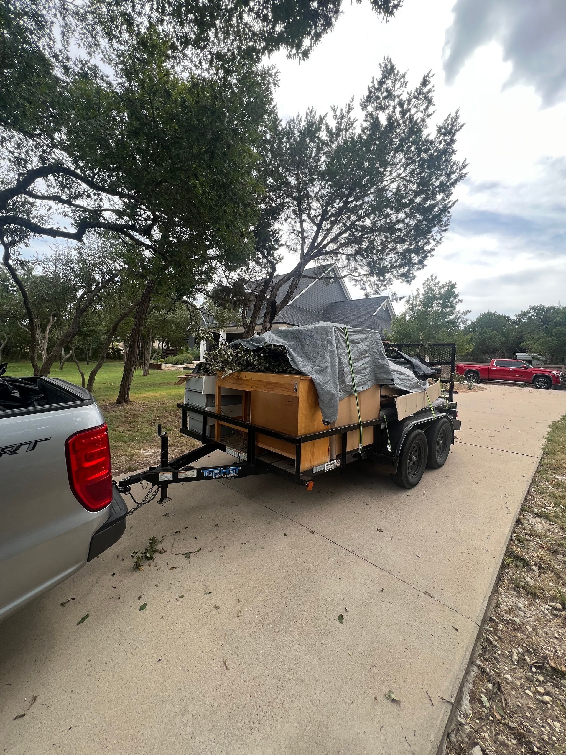 A silver truck pulling a utility trailer loaded with a tan storage chest and equipment covered by a gray tarp.