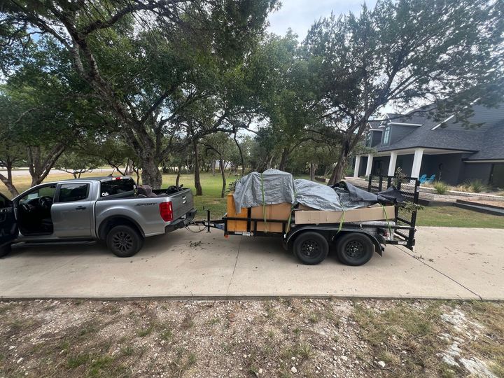 A silver pickup truck parked on a concrete driveway, towing a utility trailer loaded with covered boxes and equipment.