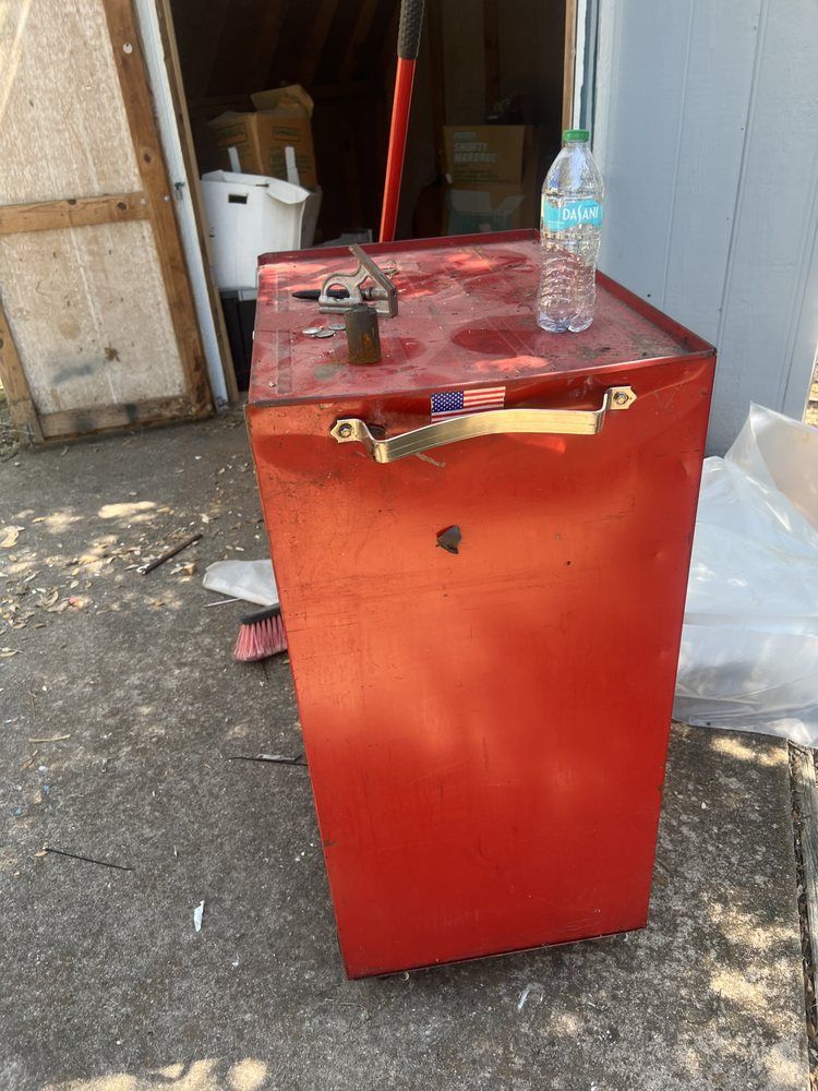 A red metal utility cabinet with a handle stands outdoors on a concrete surface, with a water bottle on top.