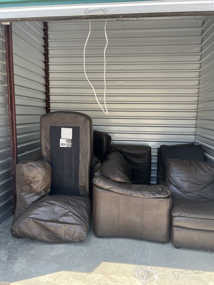 Several brown leather sofa pieces stored inside a small metal storage unit with a white cord hanging from the ceiling.