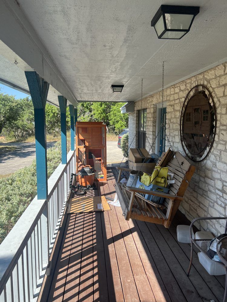 A wooden porch with blue posts, a porch swing, a wooden cabinet, and decorative stone walls under outdoor lighting.