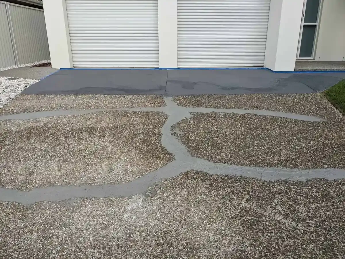 Driveway with three filled cracks; gray concrete against garage doors and lawn.