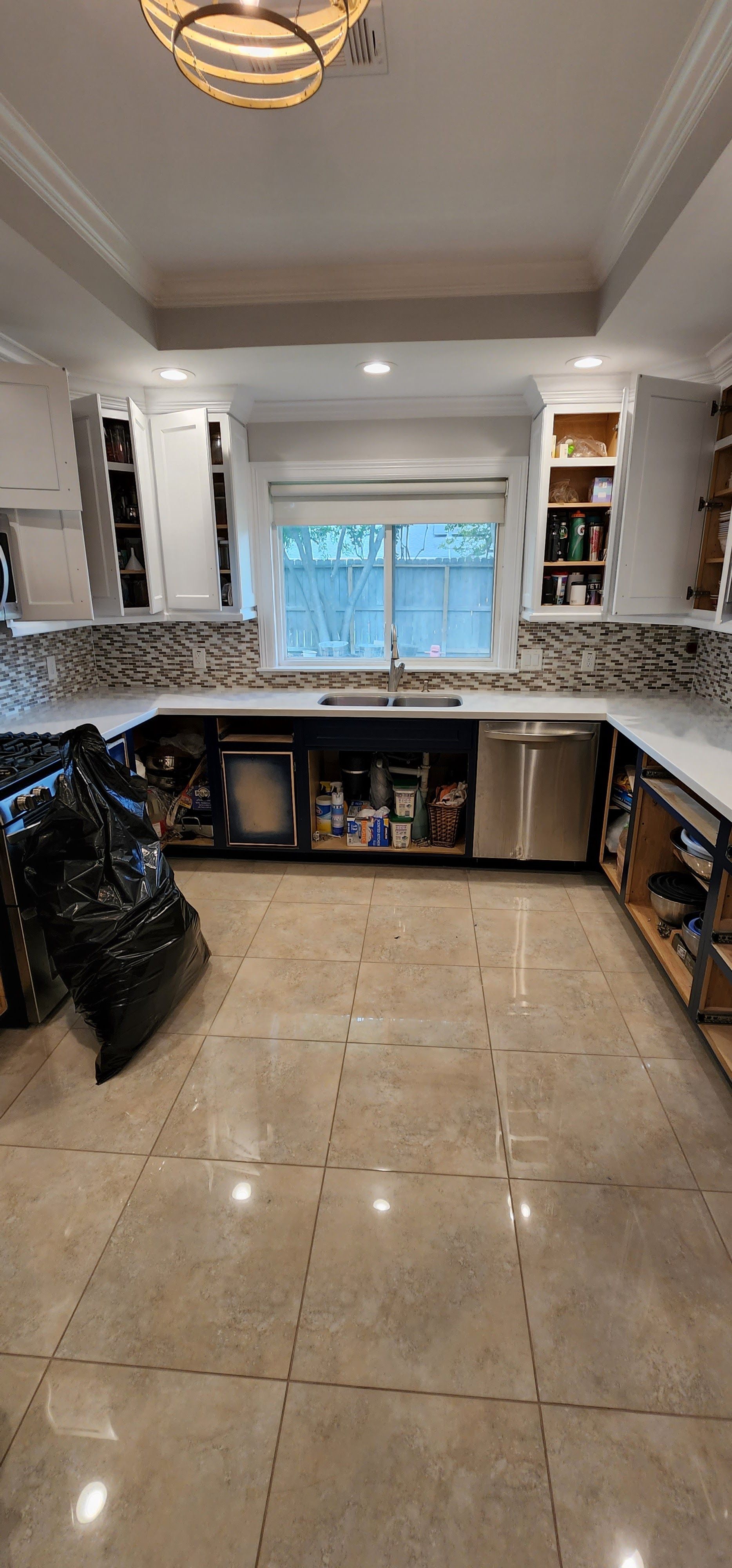 Kitchen under renovation, white cabinets, stainless steel appliances, open cabinet doors, debris on floor.