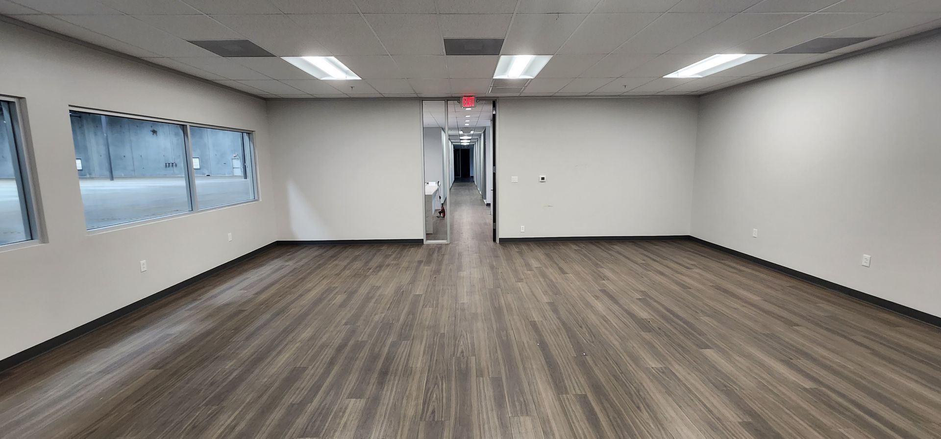 An empty office interior with a wood floor, white walls, and fluorescent lights.