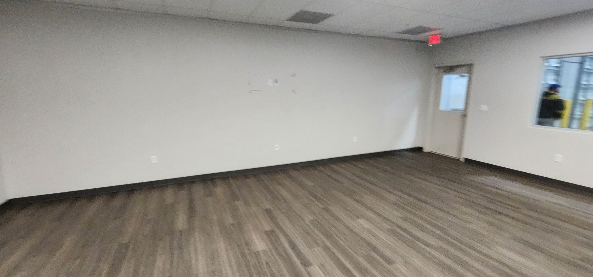 Empty room with wood-look flooring, white walls, a door, and a window.