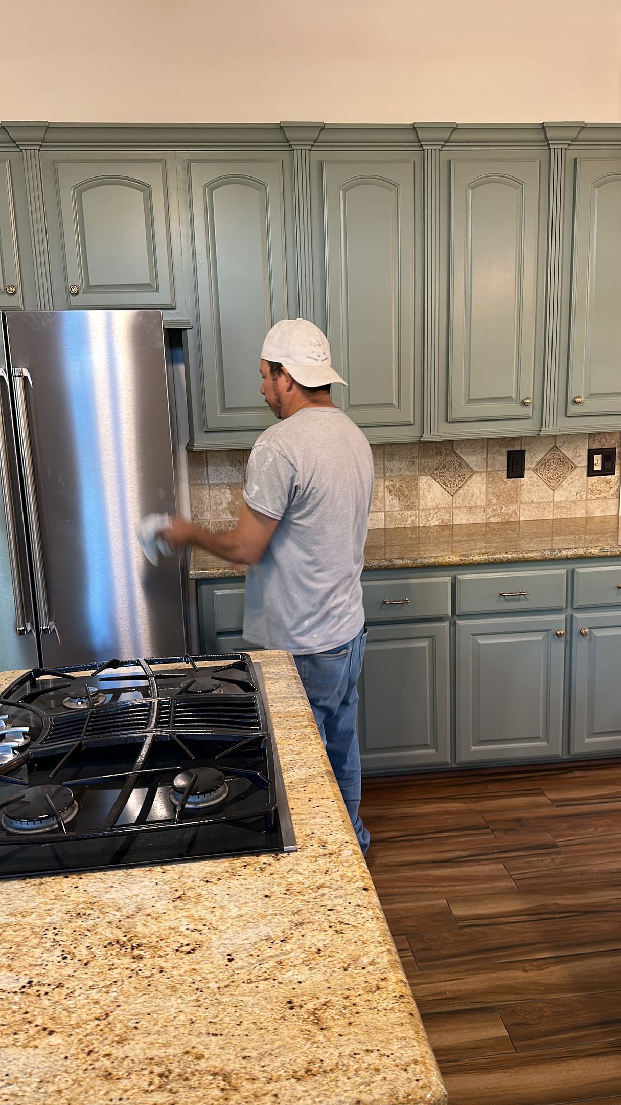 Man in a kitchen opening a stainless steel refrigerator. Blue cabinets and granite countertops are visible.