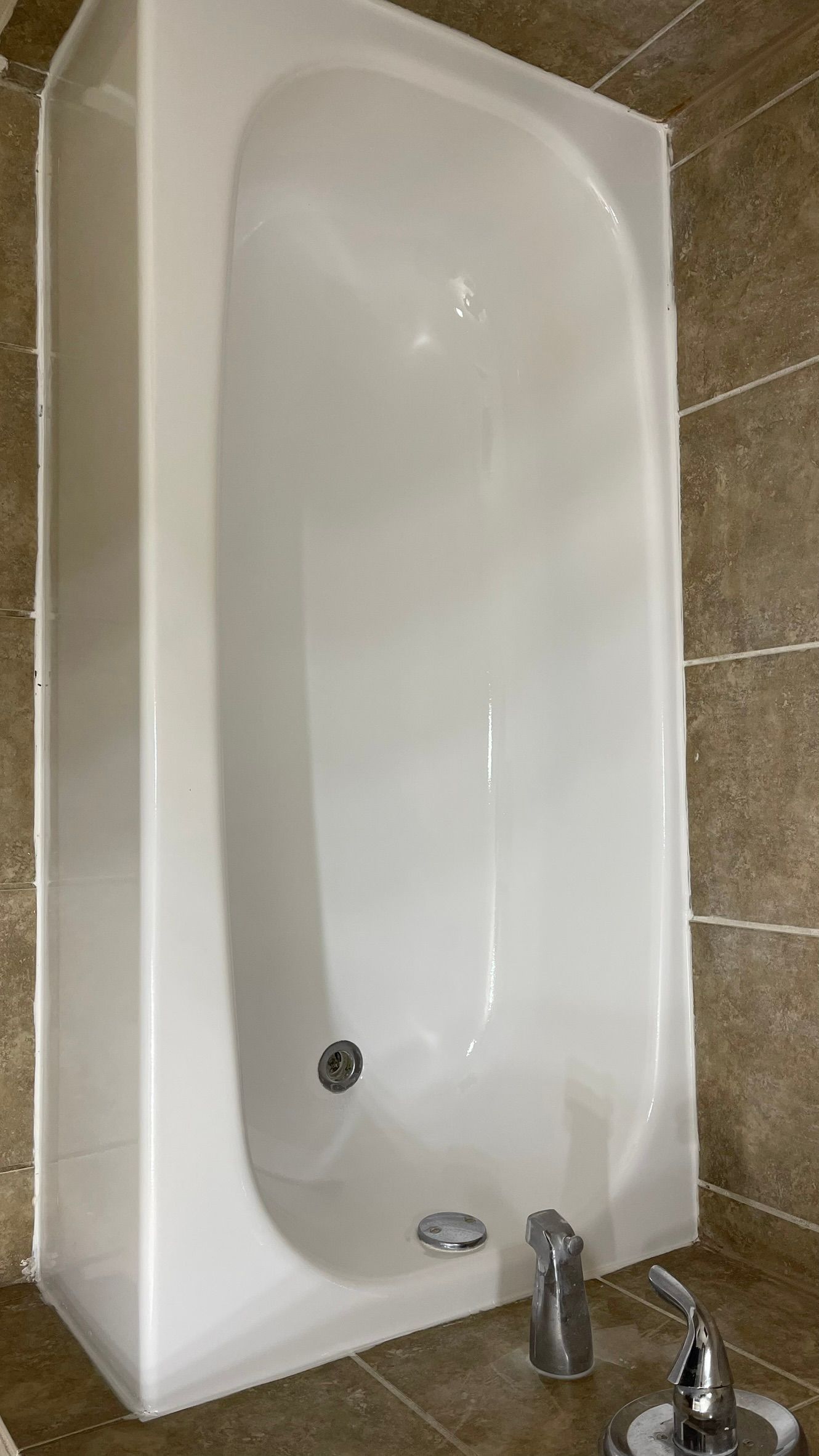 White bathtub with chrome fixtures in a bathroom, set against tiled walls and floor.