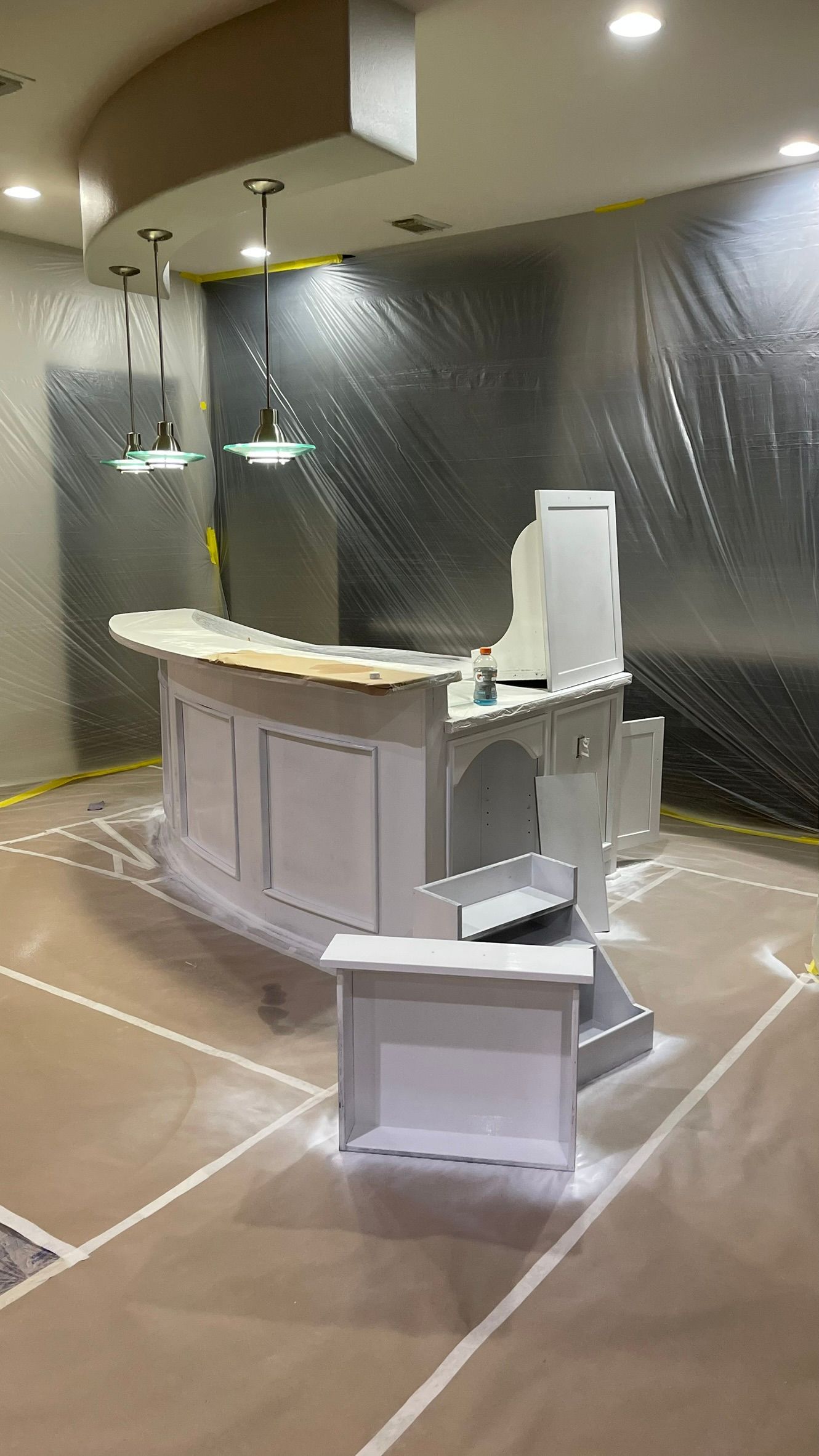 Bar area being painted, covered in plastic, with light fixtures. White paint visible on the bar.