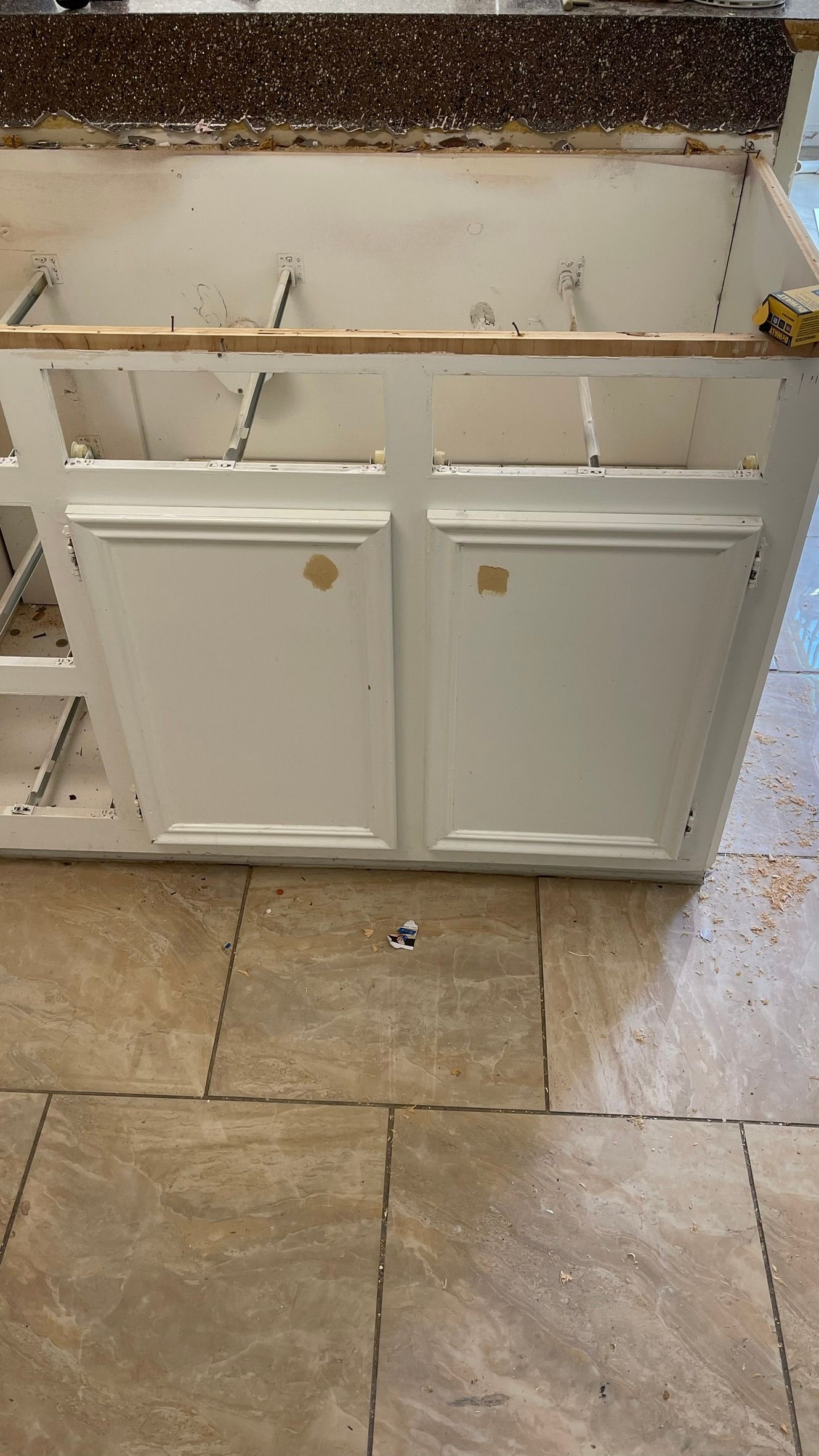 White kitchen cabinet doors with gold knobs on a tiled floor.