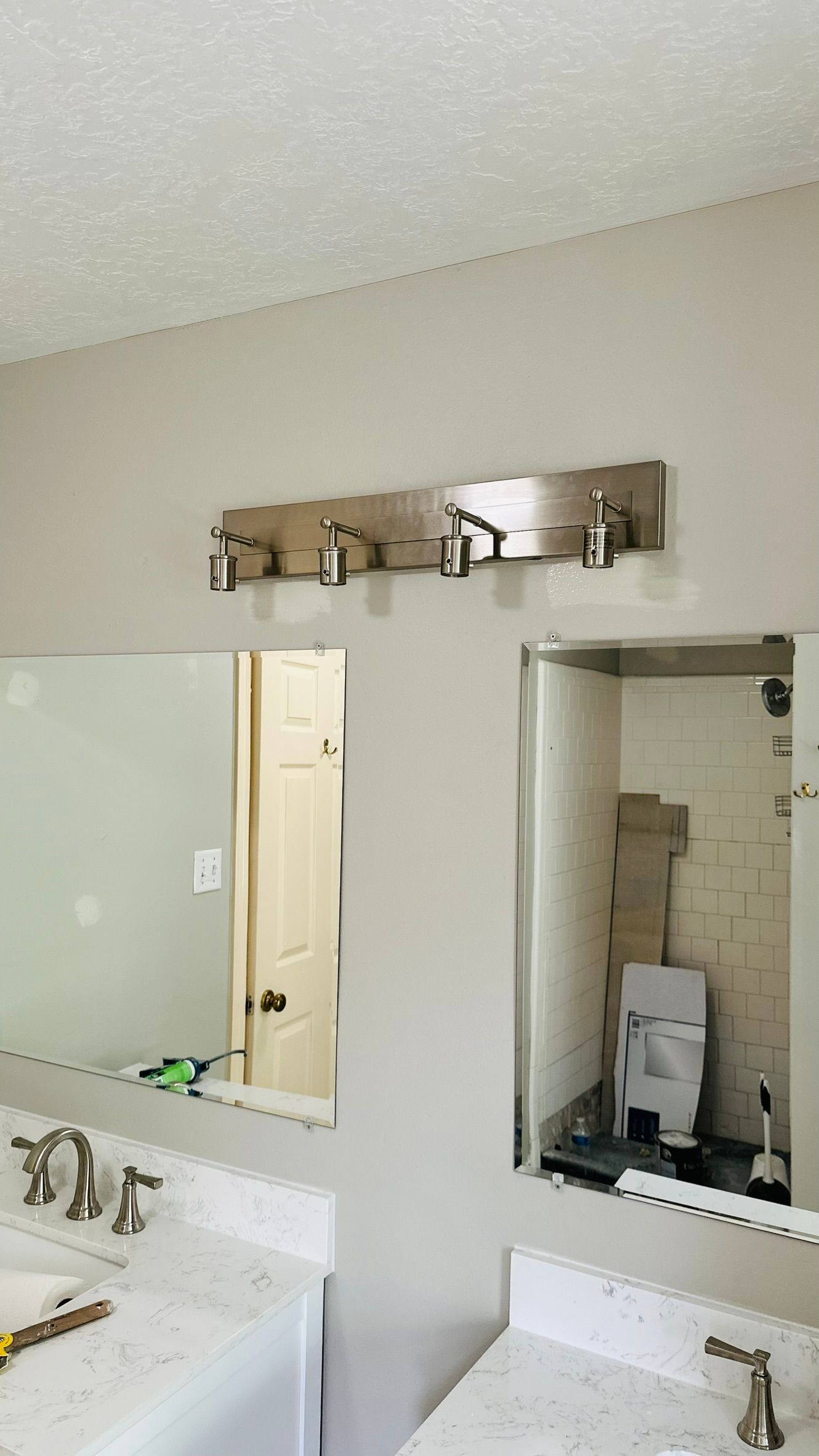 Bathroom with two mirrors, silver light fixture above, white countertops, and door visible.