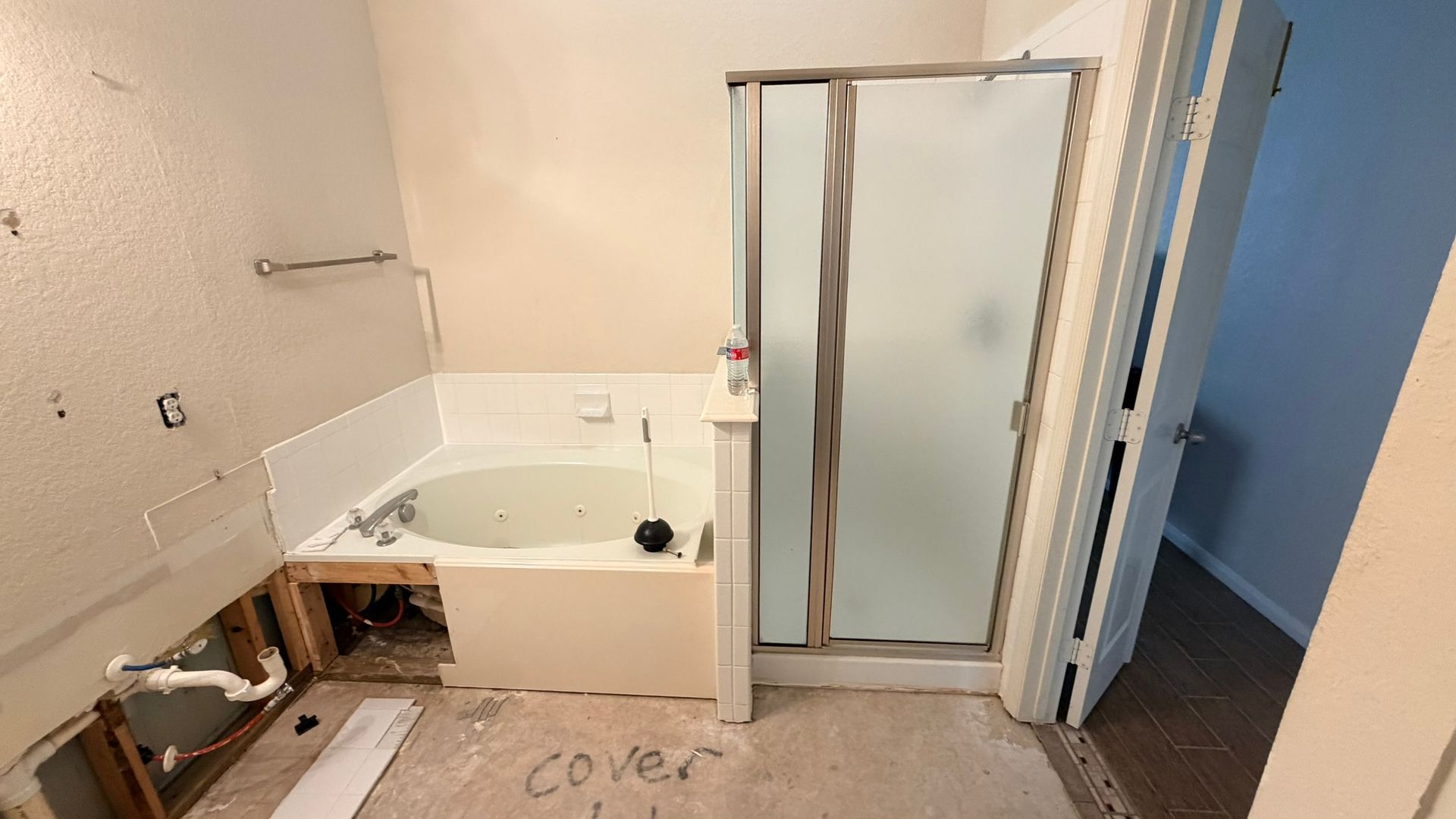 Bathroom under renovation with a white tub, glass shower enclosure, exposed plumbing, and unfinished wall panels