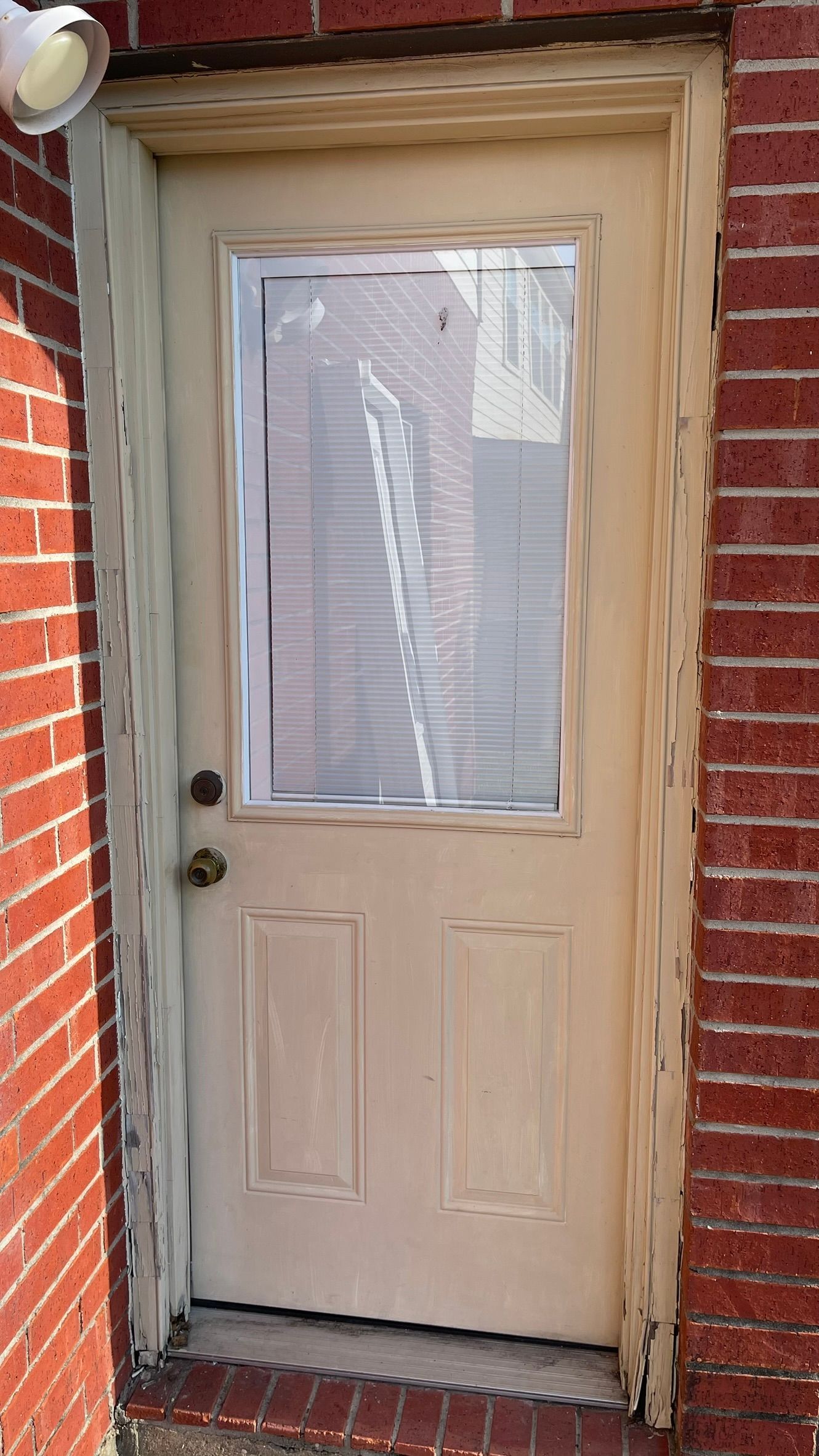 White door with glass pane in a red brick wall.