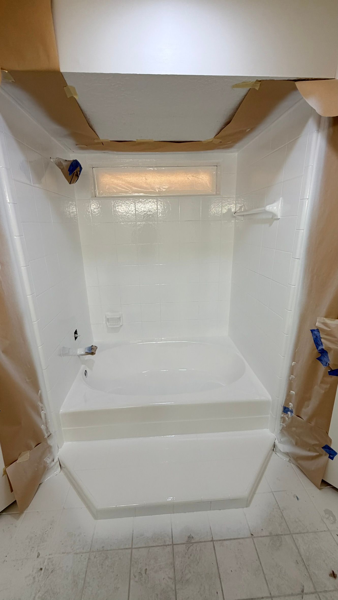 White shower stall under renovation with plastic sheeting and exposed drywall around the opening