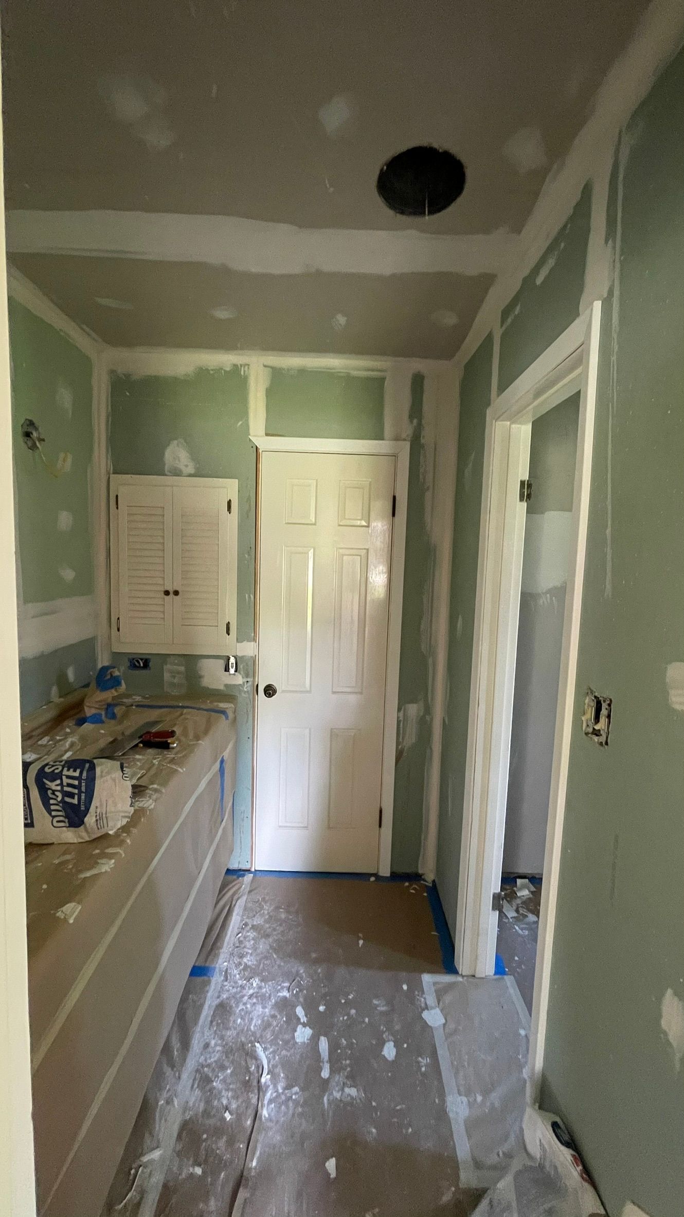 Interior view of a room under construction with green drywall and a closed white door.