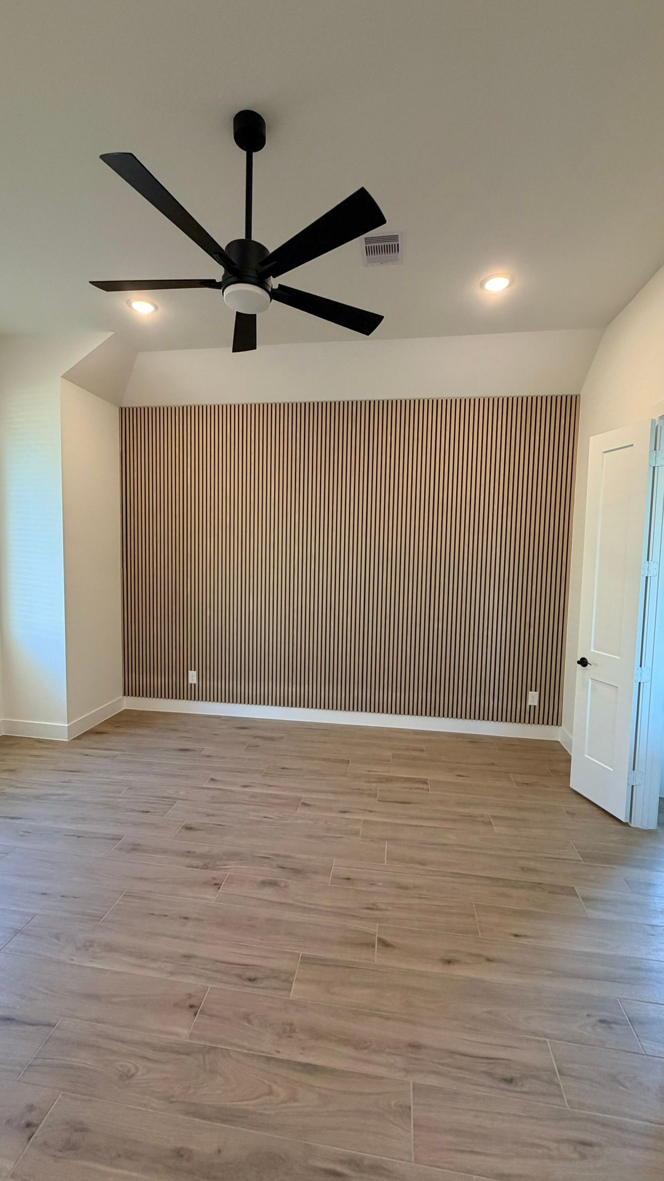 Empty room with wood floor, ceiling fan, and a striped feature wall panel.