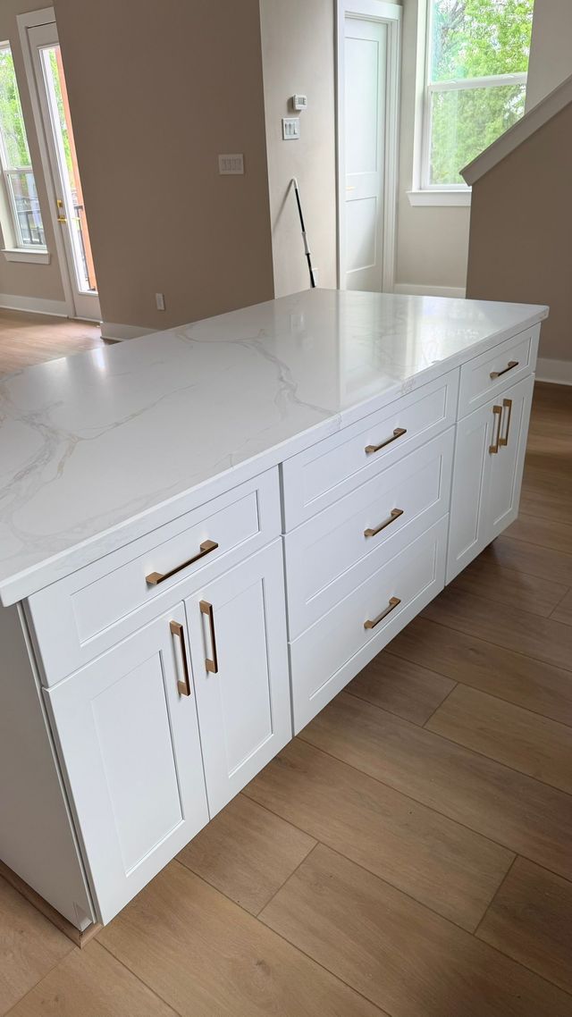 White kitchen with gold fixtures, including a faucet and cabinet hardware, and a farmhouse sink.