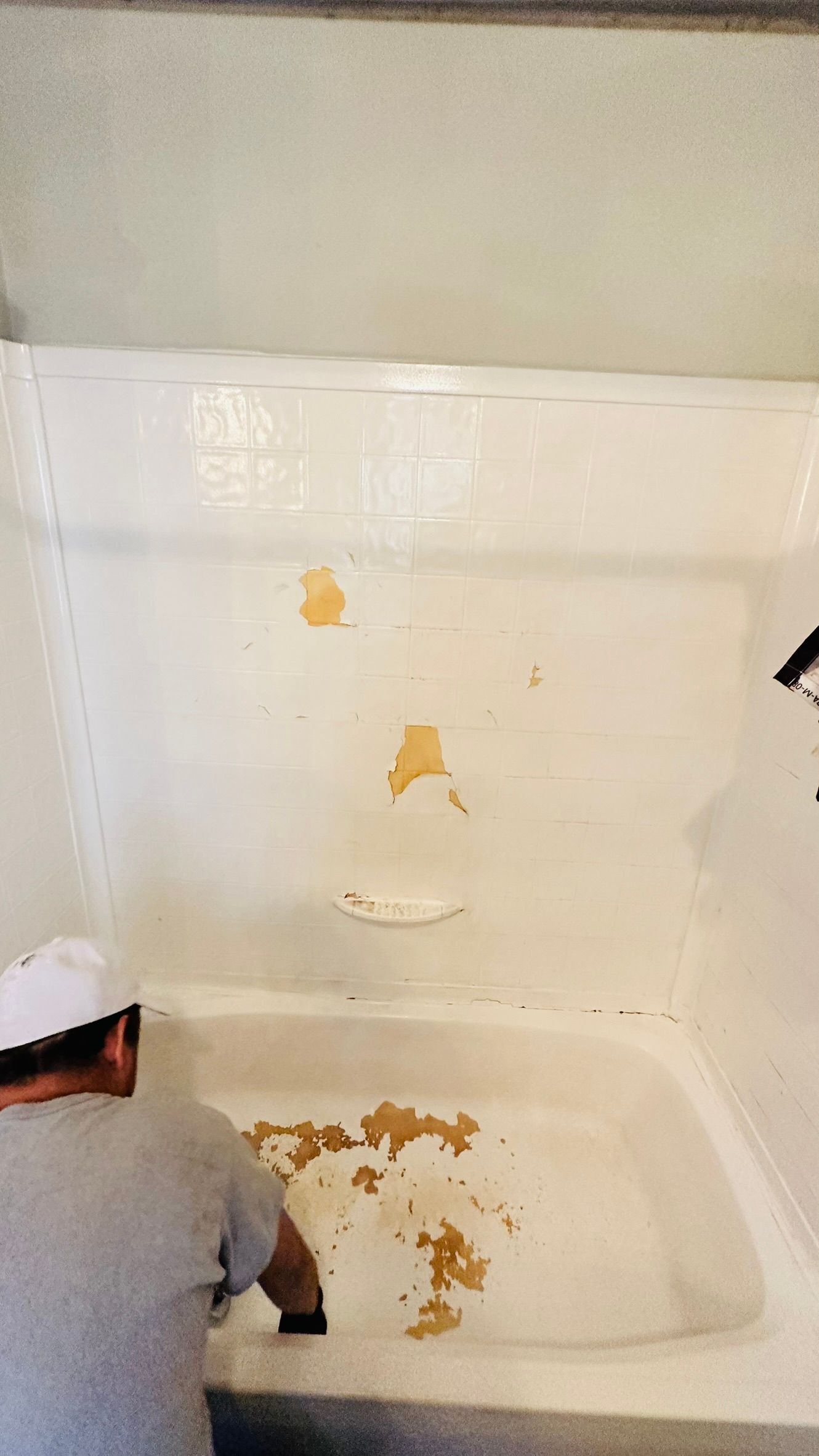 Person cleaning a white bathtub with peeling paint.