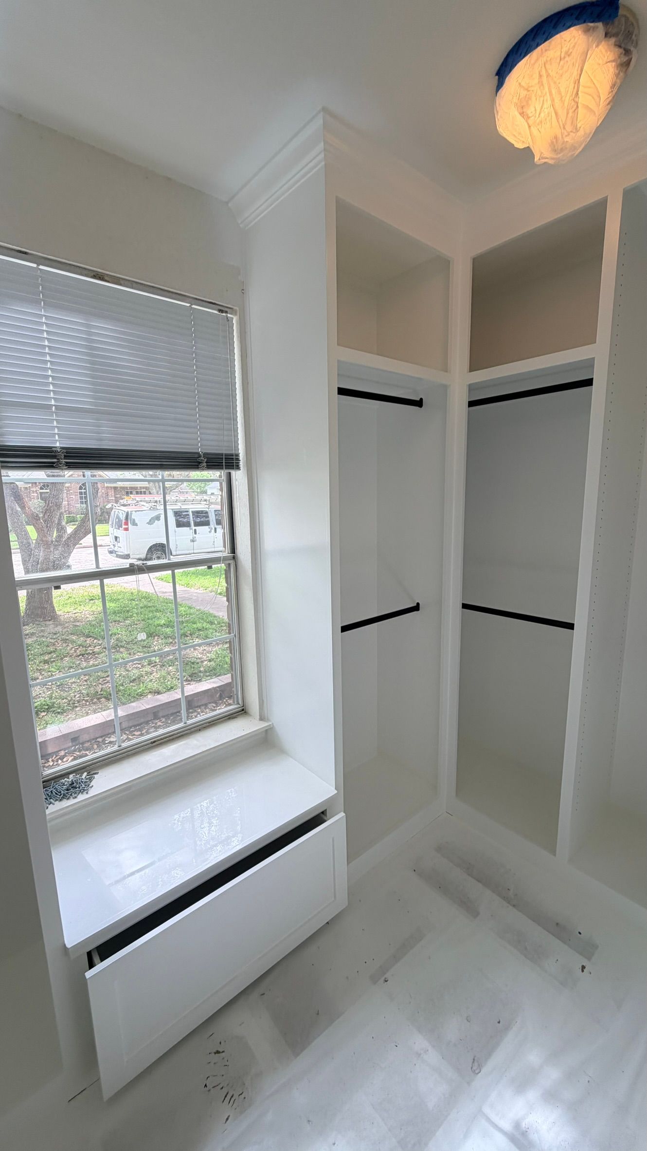 Bright white walk-in closet with shelves, hanging rods, drawers, and a window with blinds.
