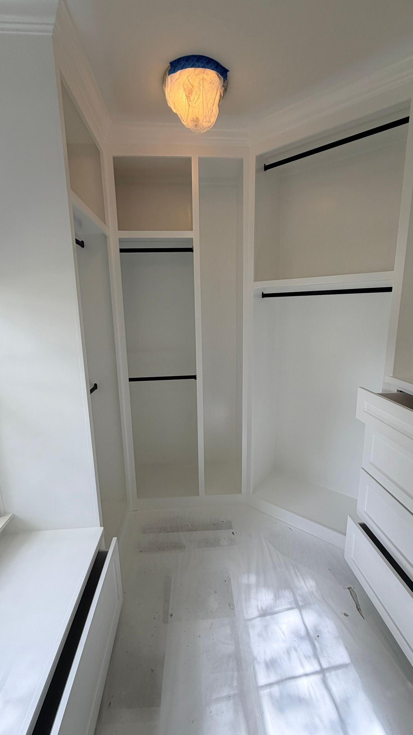 Empty white walk-in closet with built-in shelves, hanging rods, glossy tile floor, and a ceiling light.