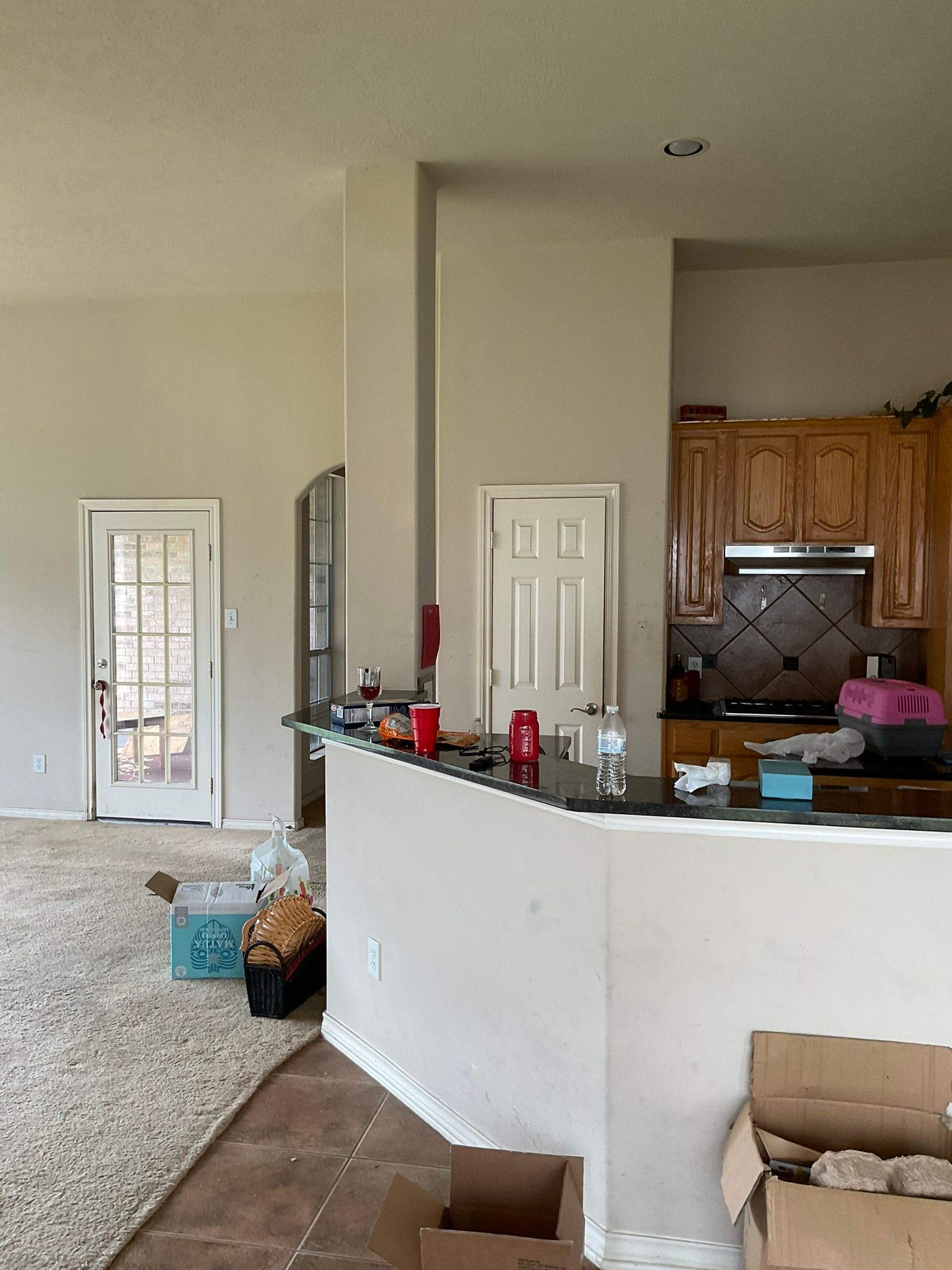 Interior view of a kitchen and living area, with a white countertop and tan cabinets.