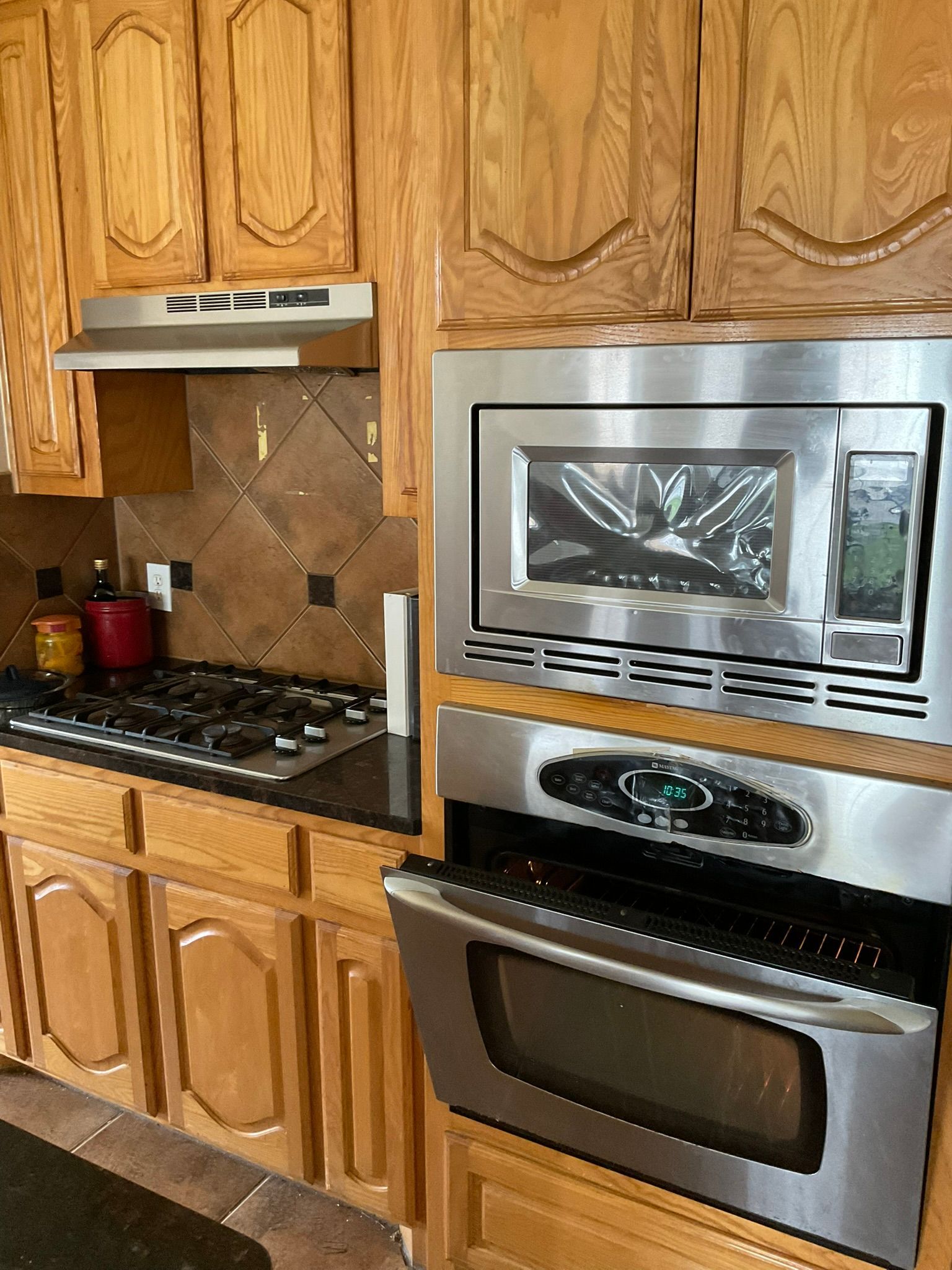 Kitchen with wooden cabinets, stainless steel oven and microwave, stovetop, and tile backsplash.