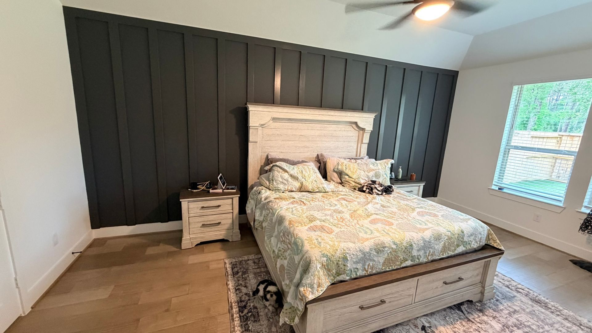 Bedroom with a bed, dark accent wall, white nightstand, ceiling fan, and window light