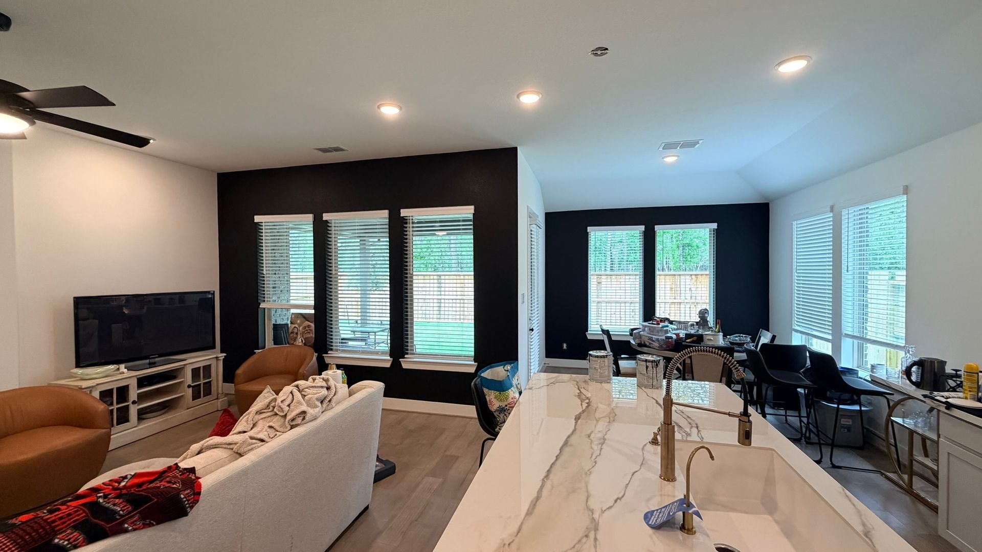 Modern open-concept living room and kitchen with white furniture, dark accent wall, and large windows.