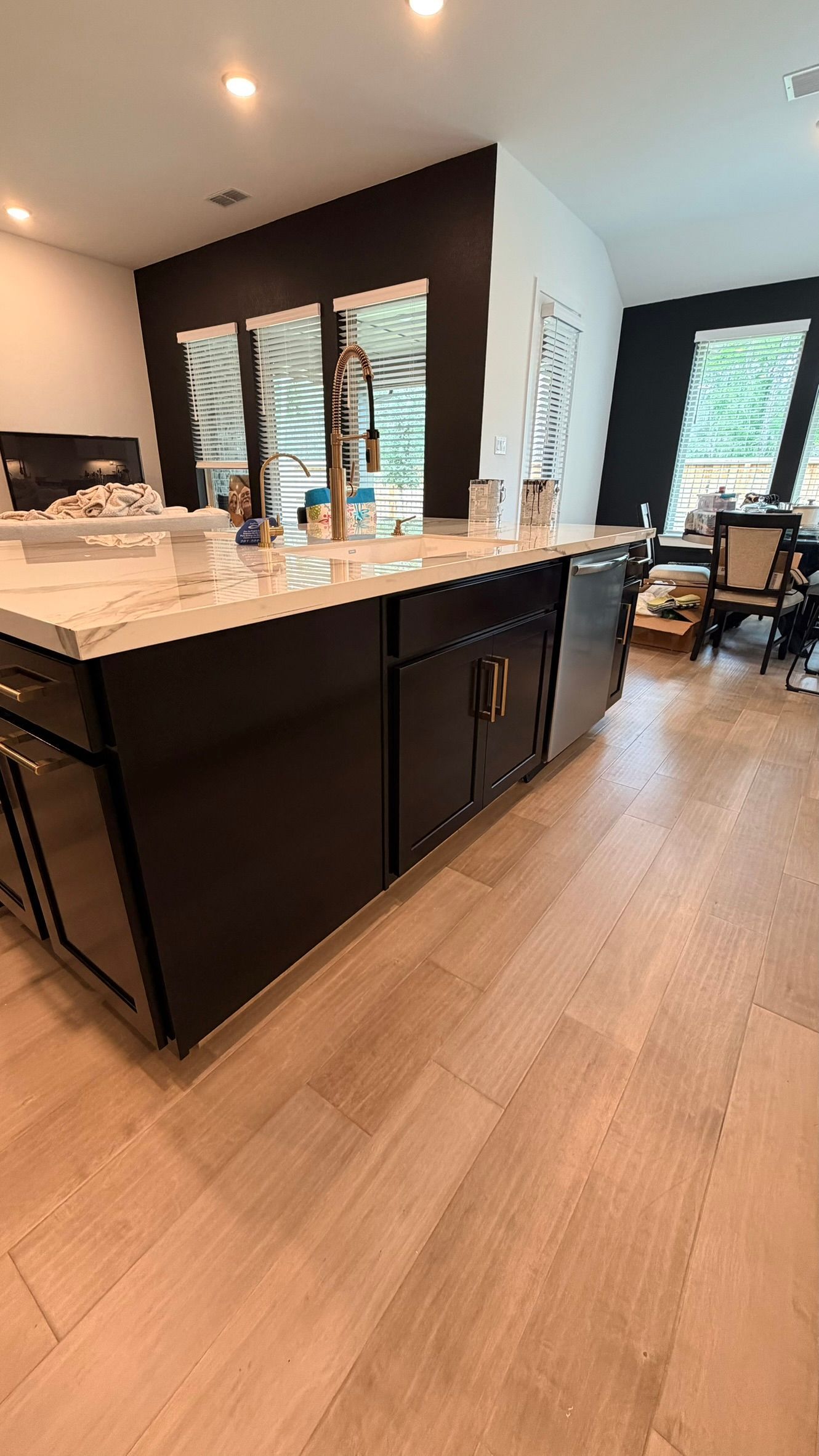 Modern kitchen with dark island, white countertops, wood floors, and large windows overlooking greenery
