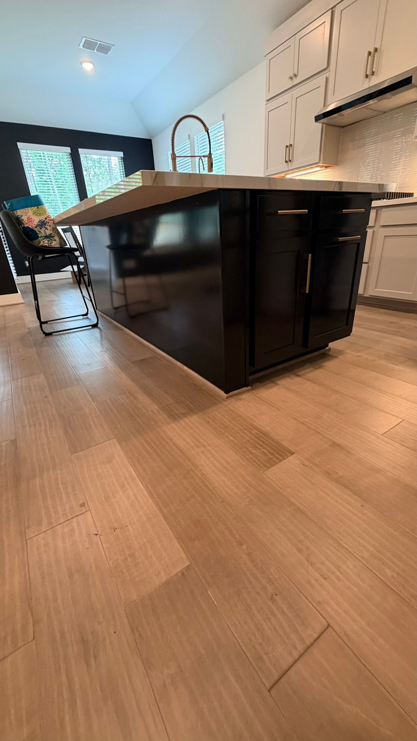 Modern kitchen with a large dark island, light wood floor, and white cabinetry, seen from low angle