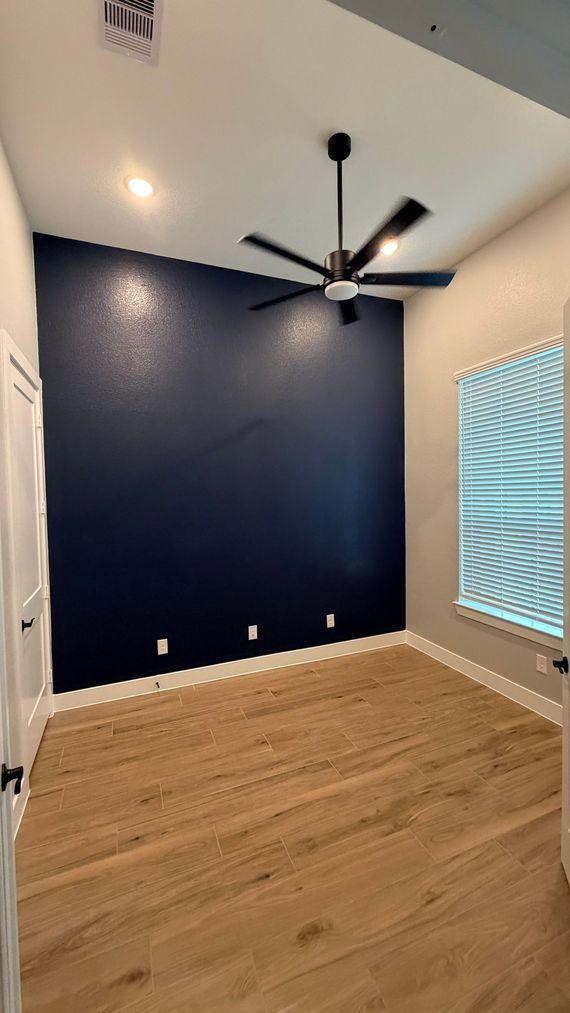 Person applying blue painter's tape to a wall corner with a paintbrush in hand.