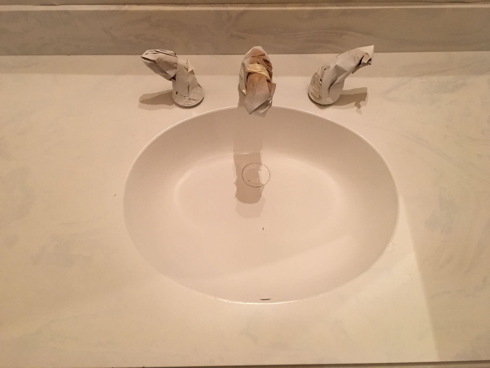 White oval sink with three faucet handles on a white countertop.