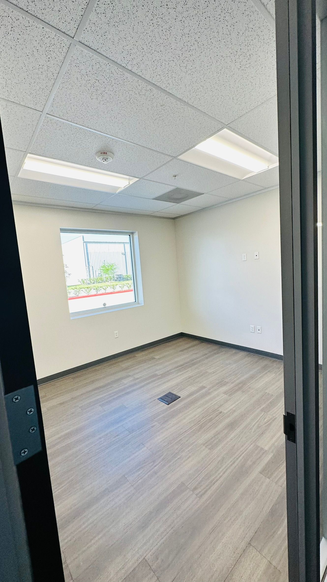 Empty office room with wood-look flooring, a window, and fluorescent ceiling lights.